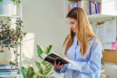 Genç ve güzel bir bayan evde kitap, roman ve edebiyat okuyor. Hobi, öğrenme, eğitim, zihinsel gelişim, gençlik kavramı