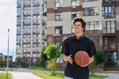 Sırt çantalı, basketbol topu dışarıda yürüyen, modern şehir geçmişi olan yakışıklı üniversite öğrencisi. Gençlik, aktif yaşam tarzı, şehir tarzı konsepti