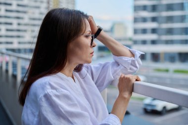 Üzgün, stresli, olgun bir kadın, açık hava portresi. Orta yaşlı ciddi bir kadın, şehir geçmişi var. Depresyon, stres, sorunlar, zorluklar, zihinsel sağlık kavramı