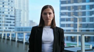 Çapraz kollu, siyah takım elbiseli, açık ofis arka planında kameraya bakan zarif, kendine güvenen bir iş kadınının portresi. İş, iş, gençlik kavramı