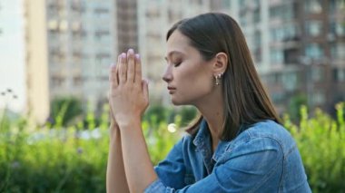 Endişeli, sinirli, genç bir kadın dışarıda yüzünü kapatıyor. Gergin, stresli, elleri dua meditasyonunda katlanmış, profil görünümlü kadın. Akıl sağlığı, olumsuz duygular, yaşam tarzı