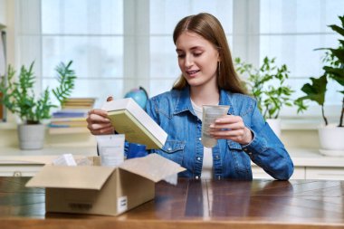 Tatmin olmuş genç bayan müşteri evde oturmuş online alımlarla dolu karton kutuları açıyor. Kozmetik ürünleri parfümleriyle dolu kutuları açan genç bir kız. Postayla teslimat, çevrimiçi mağaza