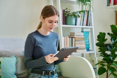 Genç bir bayan dijital tablet kullanıyor, evdeki kanepede oturuyor. Modern kablosuz teknolojiler, internet, çevrimiçi, uygulamalar, dijital aygıtlar