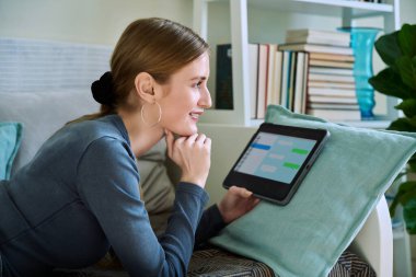 Genç bir kadının dijital tablet ekranda sohbet etmesi, rahat bir gülümseme evdeki koltukta uzanması, internet iletişimi, ulaklar, teknoloji, gençlik konsepti.