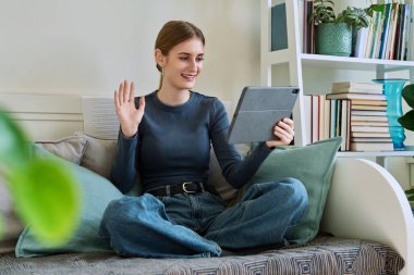 Genç kız öğrenci evde oturmuş dijital tabletin web kamerasıyla konuşuyor. 16,17,18 yaşında kız uzaktan eğitim, video konferans çağrısı, e-öğrenim teknolojisi eğitimi