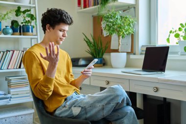 Evdeki akıllı telefondan haber okuyan mutsuz genç bir erkek. Üzgün adam üniversite öğrencisi haberleri okuyor. Sorunlar, depresyon, gençlerin akıl sağlığı