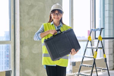 Kadın endüstriyel inşaat mühendisi mimar müfettişinin portresi. Yelek kasklı, çantalı, kameraya bakan kendine güvenen bir kadın. İnşaat teknik meslekleri