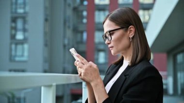 Akıllı telefon kullanan genç ciddi bir iş kadını, açık ofis binası geçmişi. Odaklanmış akıllı kadın mesajları okuyor. Teknoloji sektörü girişimciliği gençlik kavramı