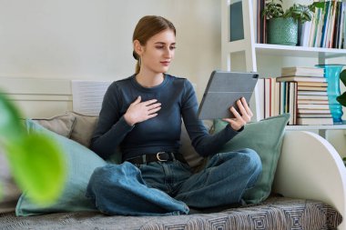 Genç kız öğrenci evde oturmuş dijital tabletin web kamerasıyla konuşuyor. 16,17,18 yaşında kız uzaktan eğitim, video konferans çağrısı, e-öğrenim teknolojisi eğitimi