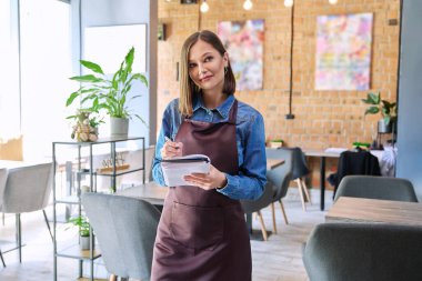 Restoran kafeteryasında, kafeteryanın iç kısımlarında çalışan, önlüklü, başarılı, genç bayan servis çalışanı. Küçük işletme işgali girişimci iş konsepti