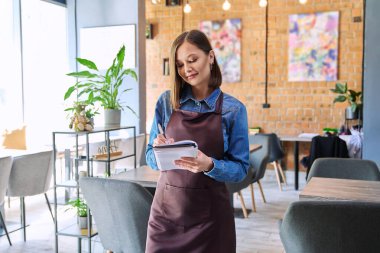 Restoran kafeteryasında, kafeteryanın iç kısımlarında çalışan, önlüklü, başarılı, genç bayan servis çalışanı. Küçük işletme işgali girişimci iş konsepti