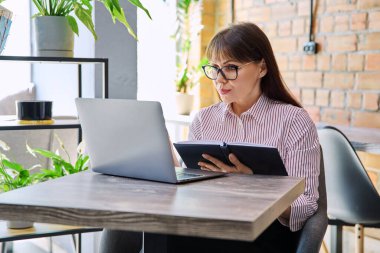 Orta yaşlı iş kadını başarılı ciddi bir kadının birlikte çalıştığı kafede dizüstü bilgisayarla uzaktan kumandayla çalıştığına inanıyor. İş, olgun insanlar, başarı, liderlik, yönetim, güçlendirme kavramı