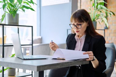 Orta yaşlı iş kadını laptopta görüntülü sohbet görüşmesi yapıyor ofis içi çalışma masasında oturuyor. Çevrimiçi iletişim teknolojisi işi, girişimcilik iş danışmanlığı