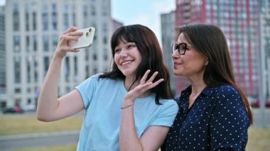 19-20 yaşlarındaki mutlu anne-kız genç, akıllı telefon webcam 'ine bakıyorlar, açık havada selfie çekiyorlar. İki nesil, aile ilişkileri arkadaşlık, anneler günü.