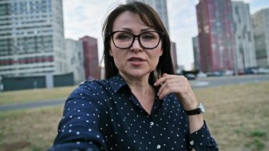 Selfie görüşü orta yaşlı iş kadını web kamerasıyla modern şehir gökdelenleri şehir tarzında konuşuyor. Ciddi kadın blogger vlogger etkileyicisi iş kadını blogu kaydediyor. Güzellik sektörü yaşam tarzı