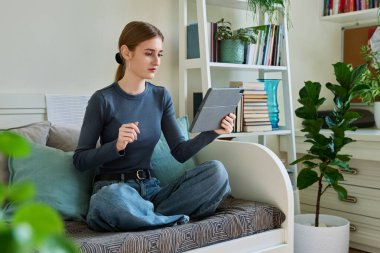 Genç kız öğrenci evde oturmuş dijital tabletin web kamerasıyla konuşuyor. 16,17,18 yaşında kız uzaktan eğitim, video konferans çağrısı, e-öğrenim teknolojisi eğitimi