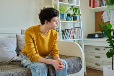 Evdeki kanepede oturan üzgün genç adam elleriyle kafasına dokunuyor. Sağlık sorunları, baş ağrıları, sorunlar, çalışmada zorluklar, aile ilişkileri, zihinsel sağlık, stres, depresyon