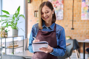 Restoran kafeteryasında, kafeteryanın iç kısımlarında çalışan, önlüklü, başarılı, genç bayan servis çalışanı. Küçük işletme işgali girişimci iş konsepti