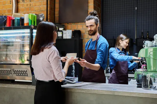 Kafede çalışan genç bir adam bir fincan kahve tezgahında bayan müşteriye servis yapıyor. İş, yemek servisi, kahve dükkanı, servis elemanı, küçük işletme konsepti