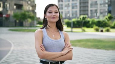 Kollarını kavuşturup şehir dışında poz veren gülümseyen güzel bir kadının portresi. 20 'li yaşlarda başarılı bir kadın. Sokak tarzı kameraya bakıyor. Gençlik yaşam tarzı güzellik insanları