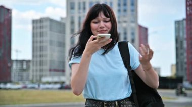 Akıllı telefondan sesli mesaj kaydeden genç bir kadın. Sesli mesaj yolluyor. Açık havada telefonla konuşuyor. Teknoloji iletişimi yaşam tarzı gençlik kavramı