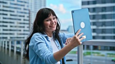 Sırt çantalı, kablosuz kulaklık takan genç bir kız öğrenci görüntülü sohbet konferansı izliyor açık hava kentindeki webcam dijital tabletinde konuşuyor. Eğitim eğlence sosyal ağları teknolojisi