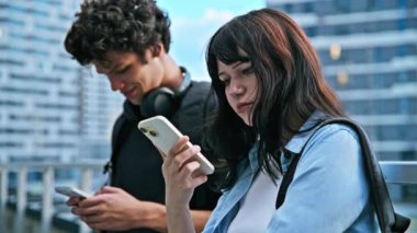 Ergen üniversite öğrencileri erkek ve kız birlikte konuşuyor, akıllı telefon kullanıyor, açık havada. 19-20 yaş arası, mobil uygulamalar teknolojiler, eğitim, yaşam tarzı, arkadaşlık kavramı.