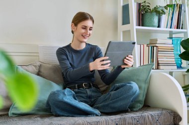 Genç kız öğrenci evde oturmuş dijital tabletin web kamerasıyla konuşuyor. 16,17,18 yaşında kız uzaktan eğitim, video konferans çağrısı, e-öğrenim teknolojisi eğitimi