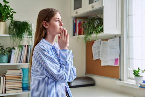 Profile view close-up of young womans face with hands folded in prayer, dreams, memories. Lifestyle, feelings, mental physical health, loneliness, stress, depression, difficulties, youth concept
