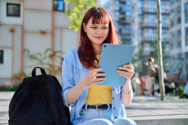 Genç çekici bayan üniversite öğrencisi dijital tablet kullanıyor, modern bina arka planı. Eğitim, teknoloji, eğitim, 19-20 yaş gençlik kavramı
