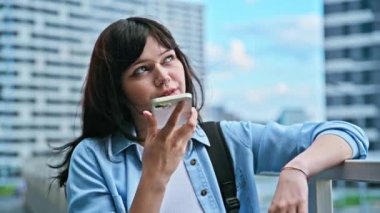 Akıllı telefondan sesli mesaj kaydeden genç bir kadın. Sesli mesaj yolluyor. Açık havada telefonla konuşuyor. Teknoloji iletişimi yaşam tarzı gençlik kavramı