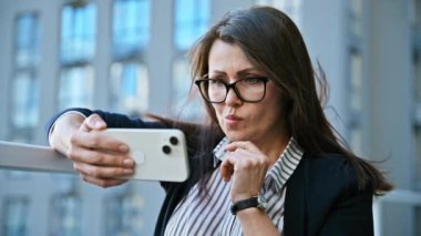 Ciddi, olgun bir kadın dışarıda akıllı telefondan video izleyip duruyor. Elinde cep telefonu olan orta yaşlı, rahat bir kadın. Yaşam tarzı, teknoloji, iş, eğitim, eğlence, 40 'lı yılların insan kavramı