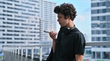 Genç adam akıllı telefondan sesli mesaj kaydediyormuş. Sesli mesaj yolluyormuş. Açık havada telefonla konuşuyormuş. Teknoloji iletişimi yaşam tarzı gençlik kavramı