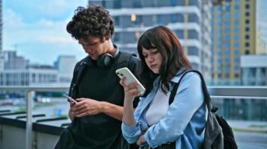Ergen üniversite öğrencileri erkek ve kız birlikte konuşuyor, akıllı telefon kullanıyor, açık havada. 19-20 yaş arası, mobil uygulamalar teknolojiler, eğitim, yaşam tarzı, arkadaşlık kavramı.