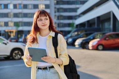 Dijital tabletli genç bir üniversite öğrencisi, açık havada. Yüz piercingli güzel kızıl saçlı kız ellerinde tutuyordu. Eğitim, teknoloji, gençlik 18-20 yıllık kavram