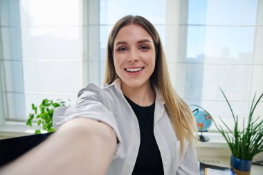 Web kamerasına bakan neşeli genç bir kadının yakın plan selfie portresi. 20-22 yaşlarındaki mutlu genç bayan. Evin içinde. Güzellik, yaşam tarzı, gençlik kavramı
