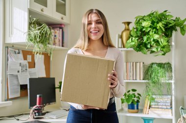Evde alışveriş yapan genç bir bayan, içinde online alışverişler olan karton kutuları açıyor. Mutlu yirmili yaşlarda kutuları açan kadın tüketiciler. Postayla teslimat, çevrimiçi mağaza, e-alışveriş konsepti