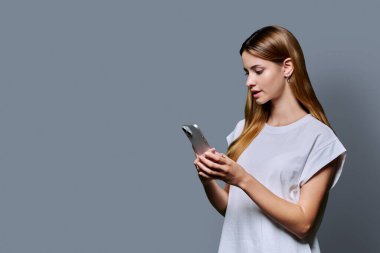 Gri stüdyo geçmişinde akıllı telefon kullanan genç ve güzel bir kadın. Moda tebessümü olan kızıl saçlı bir kadın cep telefonuna bakıyor. Teknolojiler mobil uygulama hizmetleri gençlik kavramı