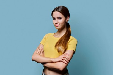 Mavi stüdyo arka planında çapraz kolları olan güzel, mutlu, modaya uygun kızıl saçlı bir kızın portresi. Kendine güvenen, gülümseyen, sarı elbiseli genç bir kadın. Güzellik, yaşam tarzı, gençlik kavramı