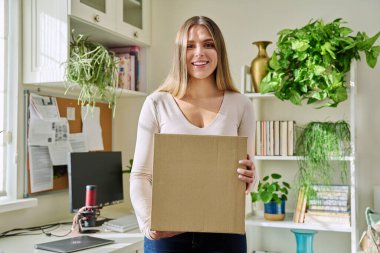 Evde alışveriş yapan genç bir bayan, içinde online alışverişler olan karton kutuları açıyor. Mutlu yirmili yaşlarda kutuları açan kadın tüketiciler. Postayla teslimat, çevrimiçi mağaza, e-alışveriş konsepti