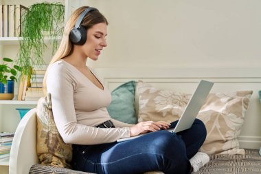 Kulaklıklı, dizüstü bilgisayar kullanan genç ve çekici bir kadın evde, kanepede oturuyor. Bayan üniversite öğrencisi, ders çalışıyor, rahatlıyor, video dinliyor, sınıf arkadaşlarıyla uzaktan görüşüyor.