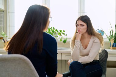 Üzgün, mutsuz, depresyondaki genç bir kadın hasta, kadın psikiyatrist psikologla terapide. Psikoloji, psikoterapi, tedavi yardım desteği, gençlik akıl sağlığı konsepti