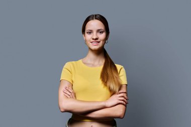 Gri stüdyo arka planında çapraz kollu güzel, mutlu, modaya uygun, kızıl saçlı bir kızın portresi. Kendine güvenen, gülümseyen, sarı elbiseli genç bir kadın. Güzellik, yaşam tarzı, gençlik kavramı