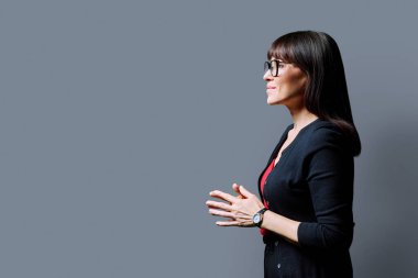 İleri bakan orta yaşlı bir kadının profil görüntüsü, gri stüdyo arka planı, reklam metni için kopya alanı. Olgun iş, kendine güvenen başarılı kadın. Pazarlama satış hizmetleri, insanlar