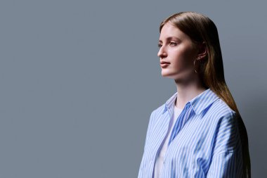 Profil görüntüsü, özgüveni yüksek genç bir kadın gri stüdyo arkaplanı arıyor, reklam metni için kopyalama alanı. Mavi tişörtlü güzel sarışın, moda stili genç.