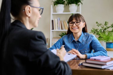 Orta yaşlı mutlu kadın hasta profesyonel bir terapistle terapi görüşmesinde. Kadın psikoterapist, gülümseyen hastayla konuşuyor. Psikoloji psikoterapisi tedaviye yardım