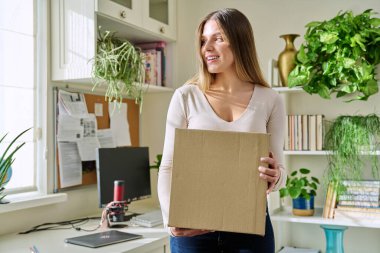 Evde alışveriş yapan genç bir bayan, içinde online alışverişler olan karton kutuları açıyor. Mutlu yirmili yaşlarda kutuları açan kadın tüketiciler. Postayla teslimat, çevrimiçi mağaza, e-alışveriş konsepti