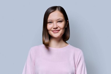 Gri stüdyo arka planında güzel bir kadının portresi. 20 'li yaşlarda çekici bir kadın kameraya bakıyor. Yaşam tarzı, bakım moda güzellik stili, iş, iş, hizmet, eğitim, gençlik