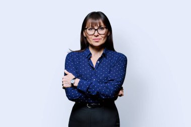 Beyaz stüdyo arka planında kollarını kavuşturmuş kendine güvenen olgun bir kadının portresi. Kameraya bakan başarılı orta yaşlı kadın. İş hayatı yaşam tarzı 40 'lı yılların insan kavramı