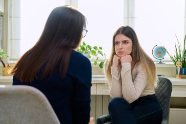 Üzgün, mutsuz, depresyondaki genç bir kadın hasta, kadın psikiyatrist psikologla terapide. Psikoloji, psikoterapi, tedavi yardım desteği, gençlik akıl sağlığı konsepti
